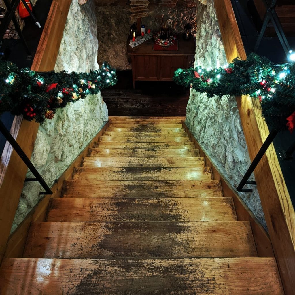Escaliers en bois du bar Ministerstwo Tajemnic décorés de guirlandes menant à une cave voûtée typique de la vie nocturne à Cracovie.