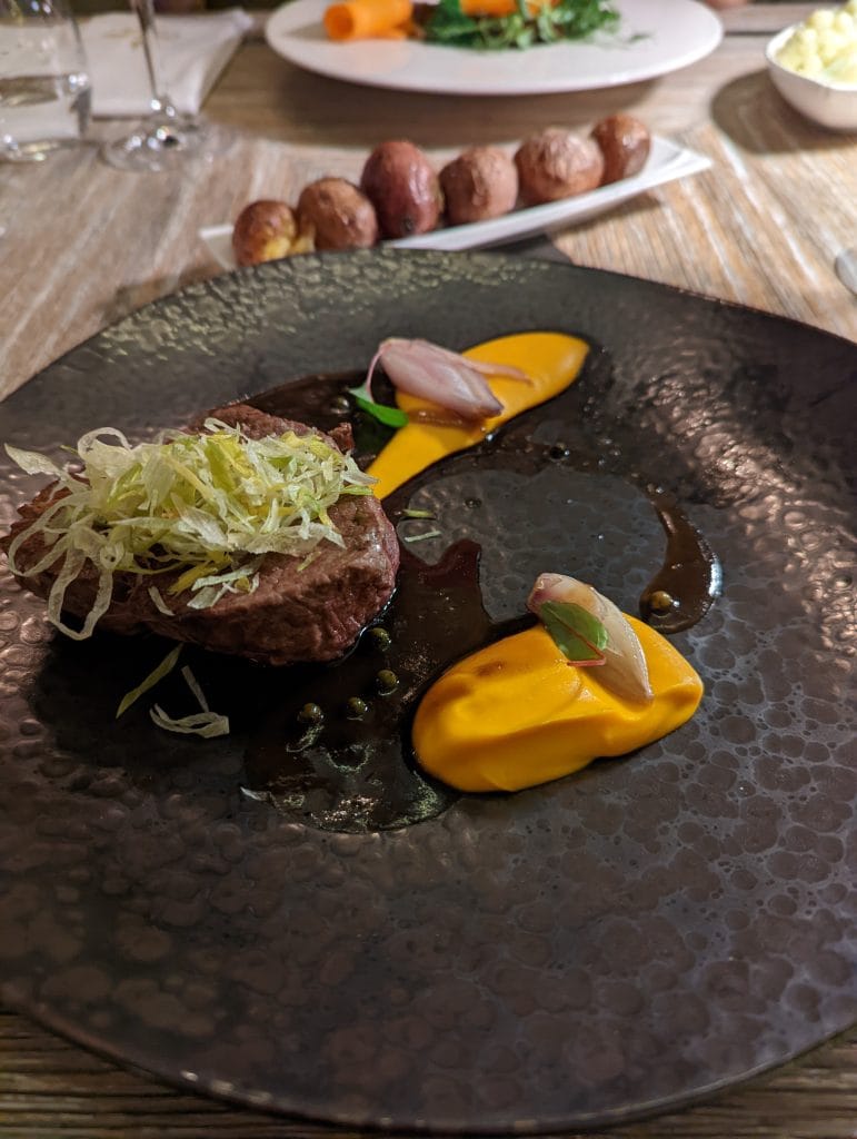 Filet de bœuf raffiné avec purée de carotte et échalotes confites, servi sur une assiette en pierre au restaurant gastronomique Szara Gęś w Kuchni.